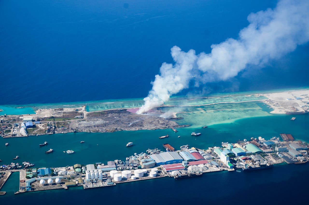 Aerial view of industrial coastline with smoke rising on a Maldivian island.