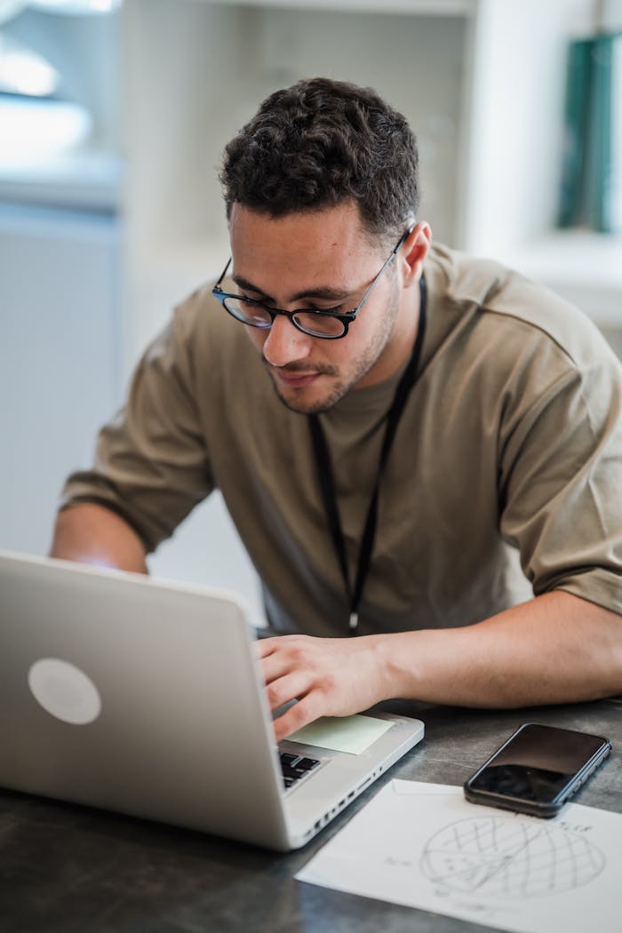 Man with eyeglasses working on laptop in a modern office setting, showcasing focused productivity.